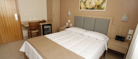 A hotel room with a bed, a desk, a chair, a nightstand, and a painting on the wall.