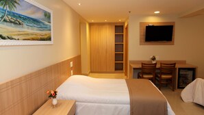 A hotel room with a bed, a desk with two chairs, a television, and a painting of a beach scene. - Elegance Praia Hotel (Rio de Janeiro)