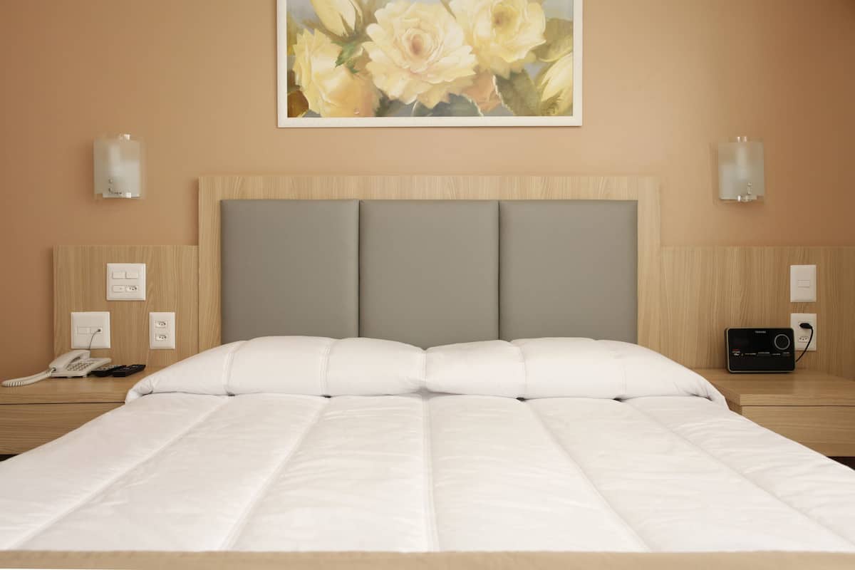 A hotel room with a large bed, a headboard with three panels, bedside tables with lamps, a phone, and a radio.