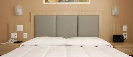 A hotel room with a large bed, a headboard with three panels, bedside tables with lamps, a phone, and a radio.