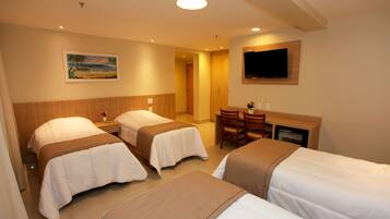 Habitación de hotel con tres camas, un televisor montado en la pared y un cuadro.