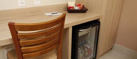 A compact kitchenette with a wooden chair, a small refrigerator, and a countertop with a basket of items.