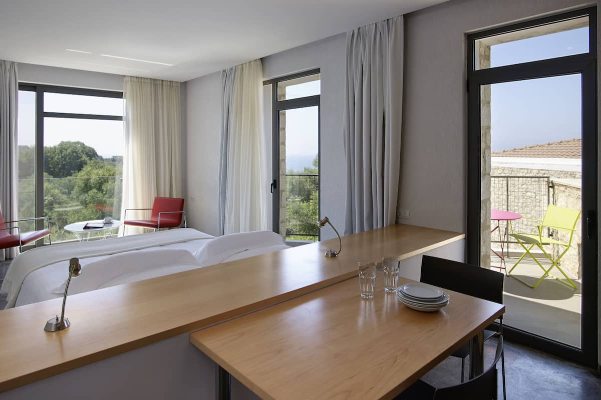 Habitación de hotel con cama, escritorio con lámpara, silla y balcón con mesa y sillas.