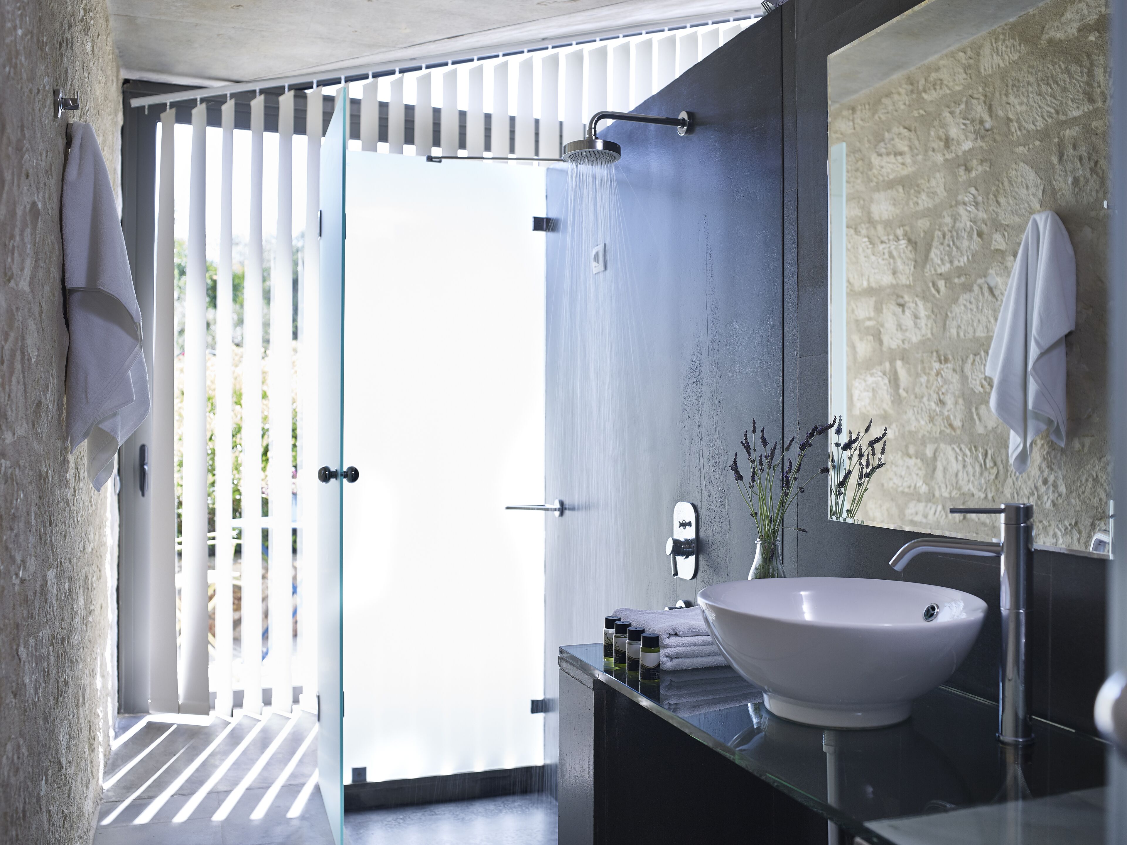 Un bagno moderno con un lavandino bianco di grandi dimensioni, un box doccia in vetro e una parete con texture in pietra.