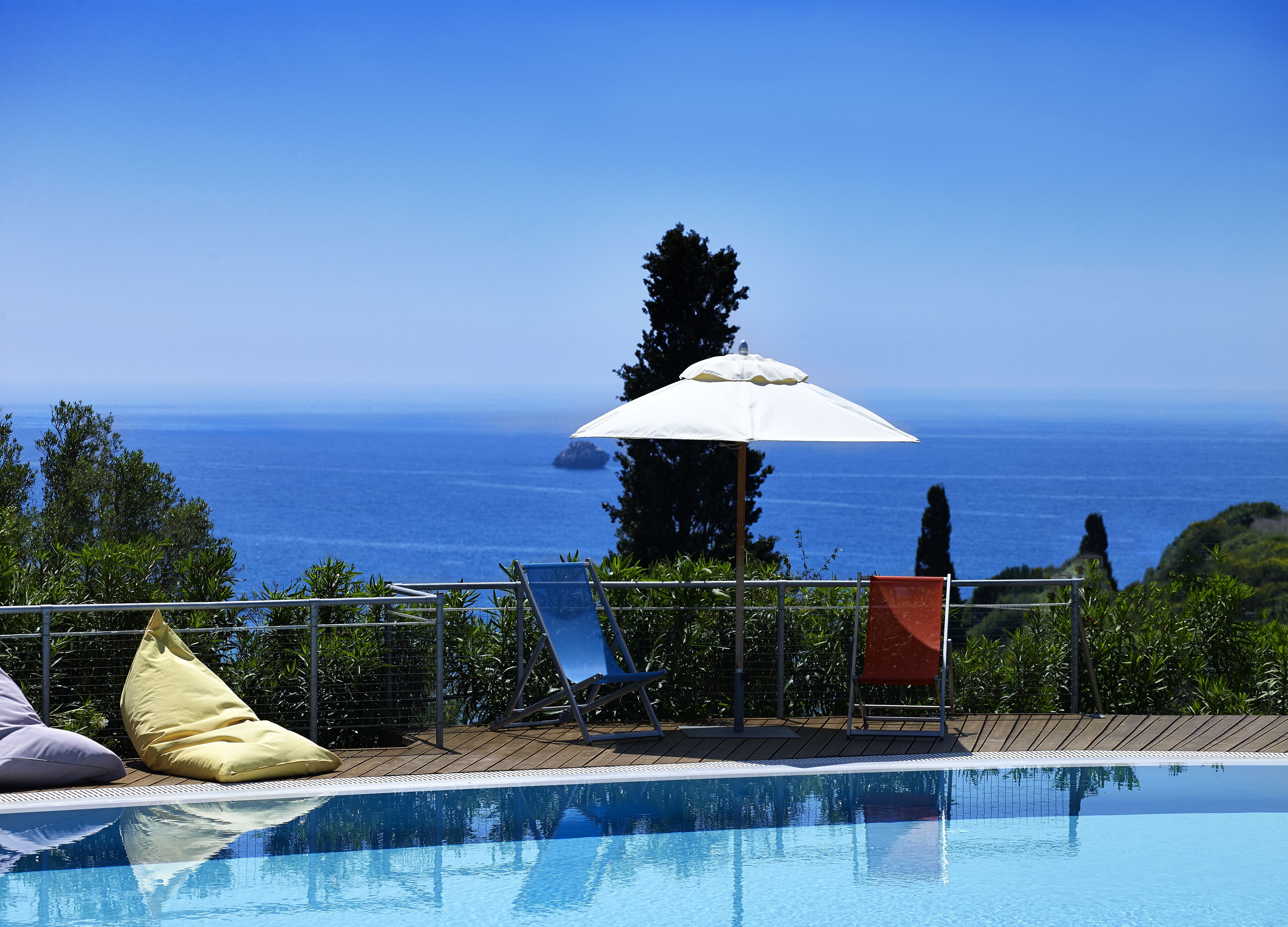 A pool with a view of the sea, a white umbrella, and a chair.