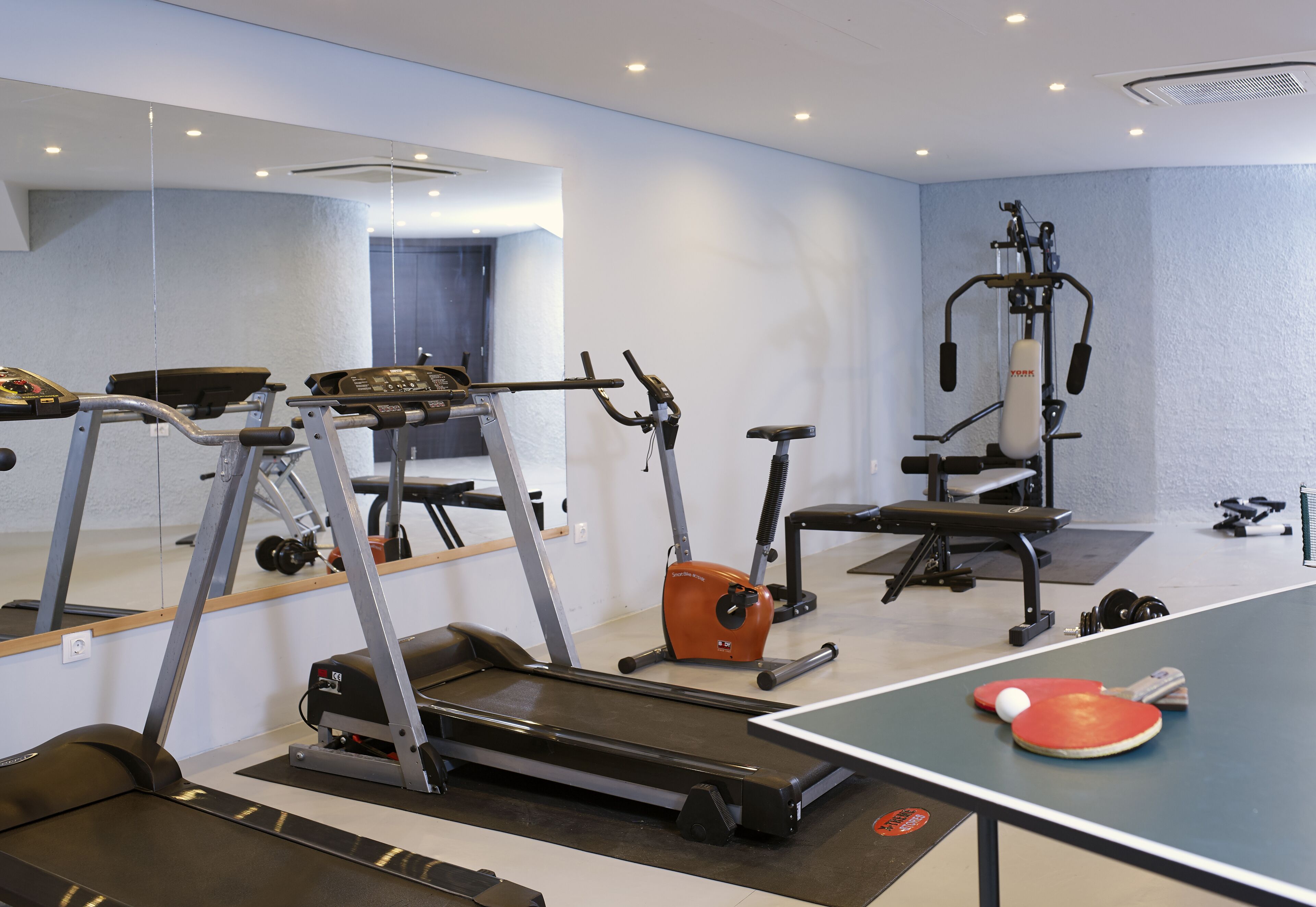 A gym with exercise equipment including a treadmill, elliptical, and weight machines.