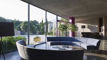 Un área de estar moderna con un sofá curvo, una mesa de centro con libros y grandes ventanales con vistas al exterior.