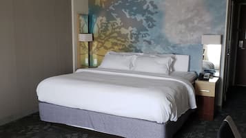 A hotel room with a large bed, a nightstand with a lamp, and a wall mural.