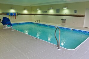 An indoor swimming pool with clear water, a lifeguard chair, and a no lifeguard on duty sign.
