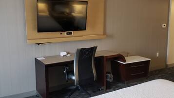 Une chambre d’hôtel comprenant un lit, un bureau avec une chaise, un téléviseur à écran plat fixé au mur et une petite poubelle.