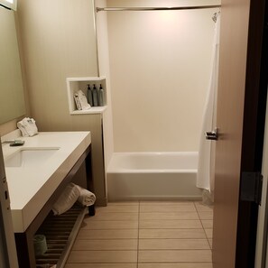 A bathroom with a white sink, a mirror, a shelf with toiletries, a bathtub, and a shower curtain.