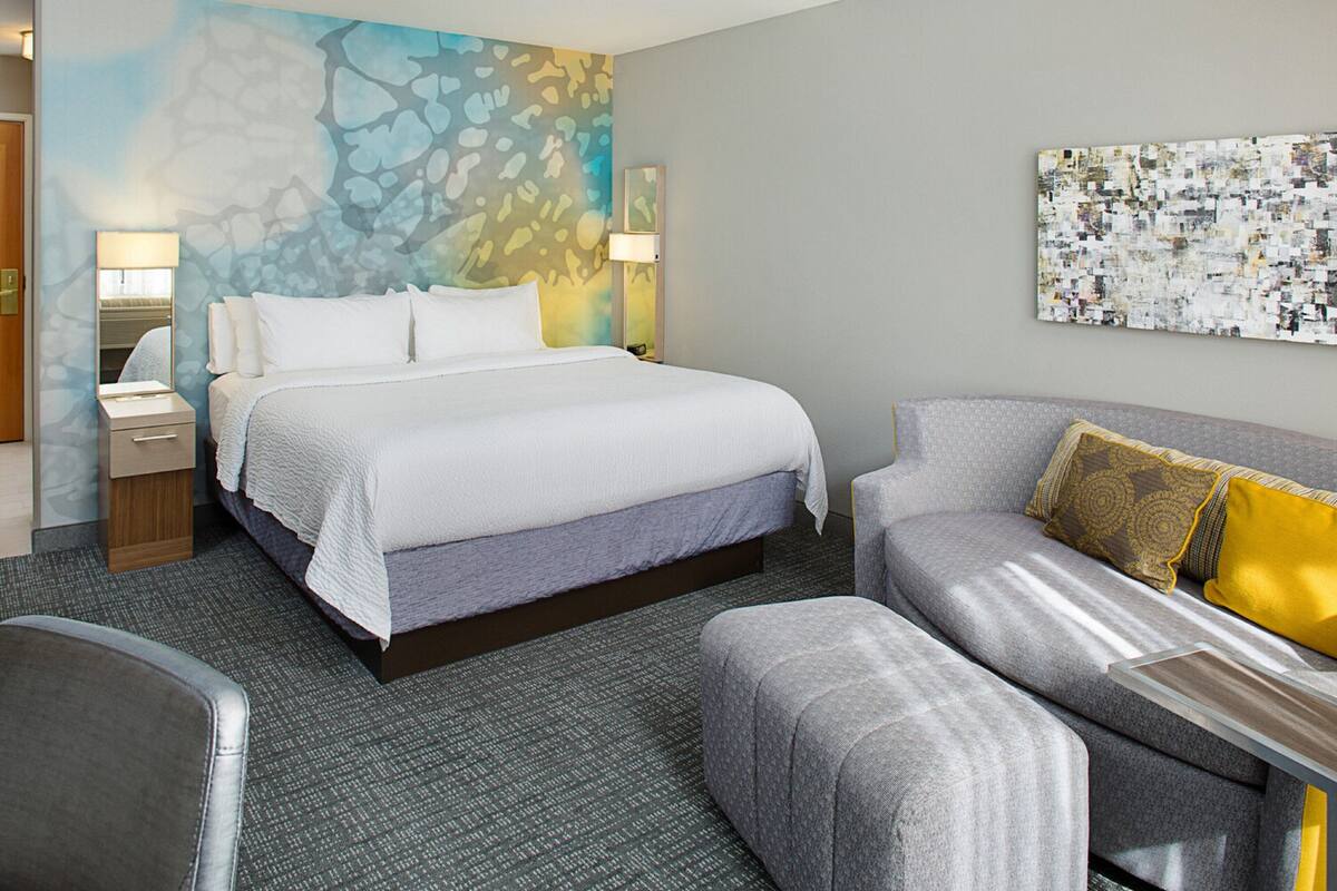 A hotel room with a bed, a sofa, a small table, and a wall with a mosaic artwork.