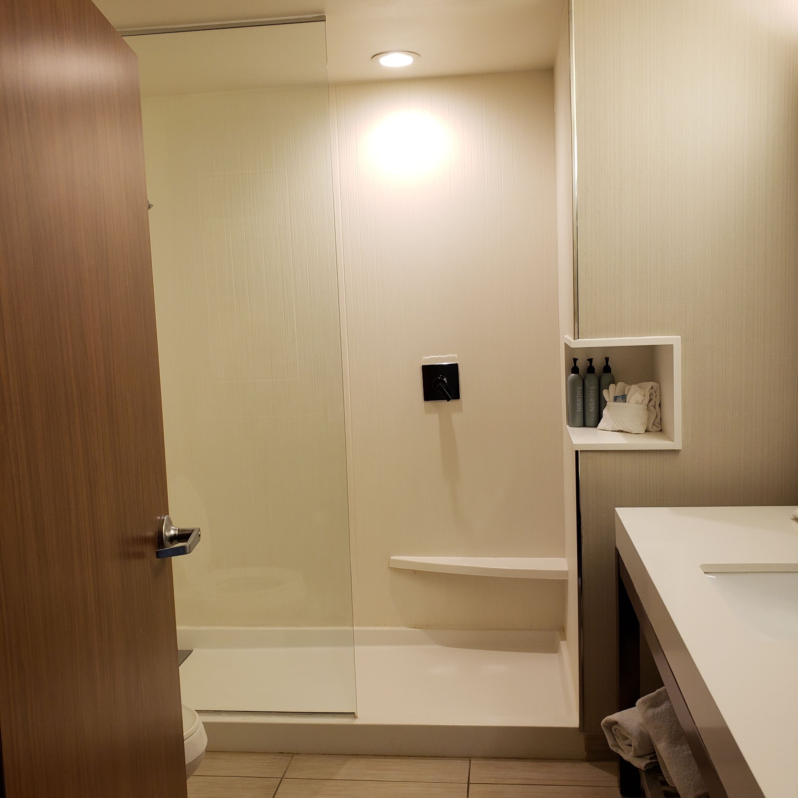 A modern bathroom with a glass shower enclosure, a white sink, and a shelf with toiletries.