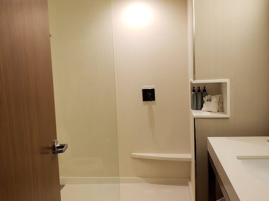 A modern bathroom with a glass shower enclosure, a white sink, and a shelf with toiletries.
