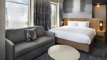 Quarto de hotel com uma cama grande, um sofá, uma mesa redonda e vista para a cidade pela janela.