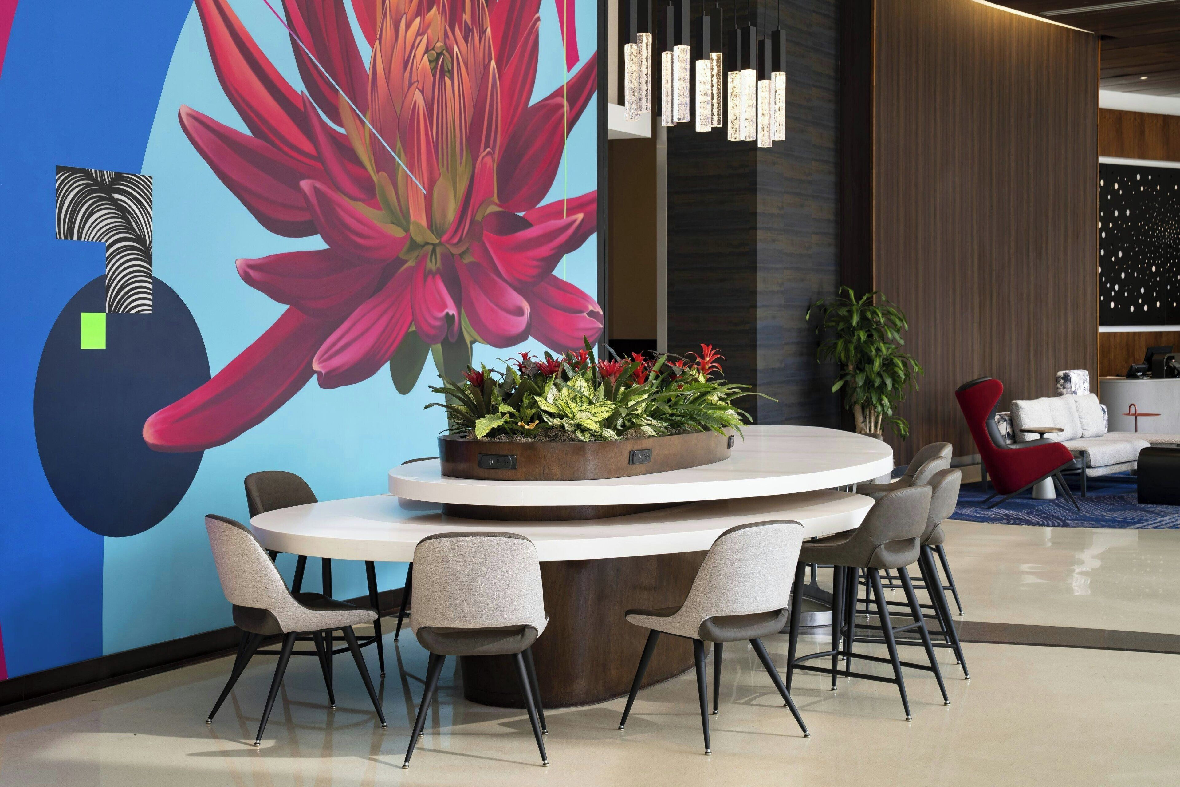 A modern interior with a round table surrounded by chairs, a large floral mural, and a vertical light fixture.