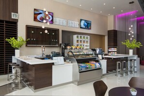 A modern cafe with a central counter, bar stools, and a display case with beverages. - Courtyard Los Angeles L.A. LIVE (Los Angeles)