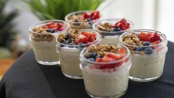 Six glass jars of yogurt topped with granola and fresh fruits on a black surface.