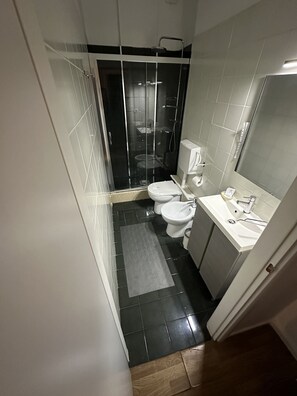 A compact bathroom with a glass shower enclosure, a toilet, and a sink.