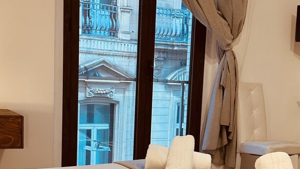 A hotel room with a bed, a window with curtains, a view of a building, and a wine glass on the floor. - B&B Degli Artisti (Lecce)