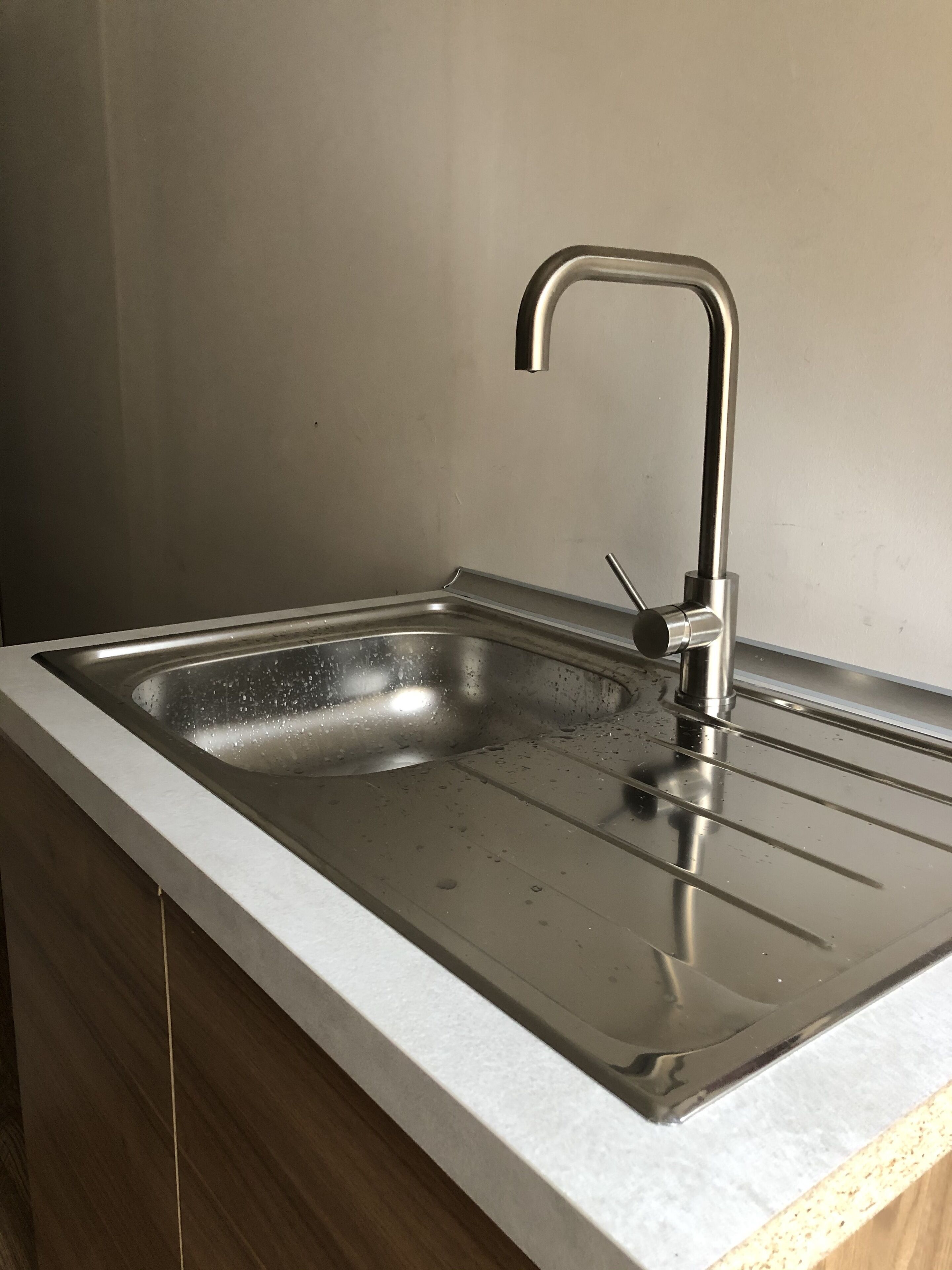 A stainless steel kitchen sink with a single faucet, a countertop, and wooden cabinets.