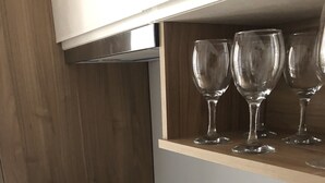 A kitchen with a black induction cooktop, wooden cabinets, and a shelf with wine glasses and ceramic cups. - B&B Degli Artisti (Lecce)
