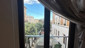 A view from a window with curtains, overlooking a street with buildings and a clear sky. - B&B Degli Artisti (Lecce)