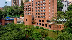 A multi-story building with a brick facade, surrounded by lush greenery and other high-rise buildings. - Hotel Dann Carlton Belfort Medellin (Medellín)