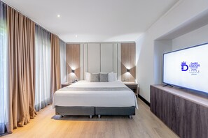 Ein modernes Hotelzimmer mit einem großen Bett, einem Holz-Kopfschild, Nachttischen, einem Flachbildfernseher und Vorhängen.