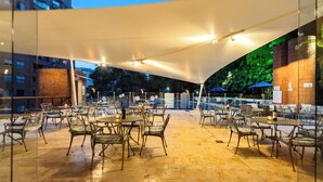 An outdoor patio area with tables and chairs, a large canopy, and a brick wall. - Hotel Dann Carlton Belfort Medellin (Medellín)
