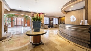A hotel lobby with a reception desk, a large potted plant, a check-in counter, and a seating area. - Hotel Dann Carlton Belfort Medellin (Medellín)