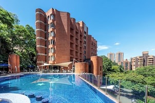 Un hotel con piscina, fachada de ladrillo y abundante vegetación.