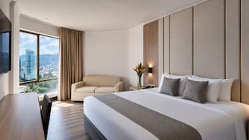 A hotel room with a large bed, a sofa, a desk, and a TV.