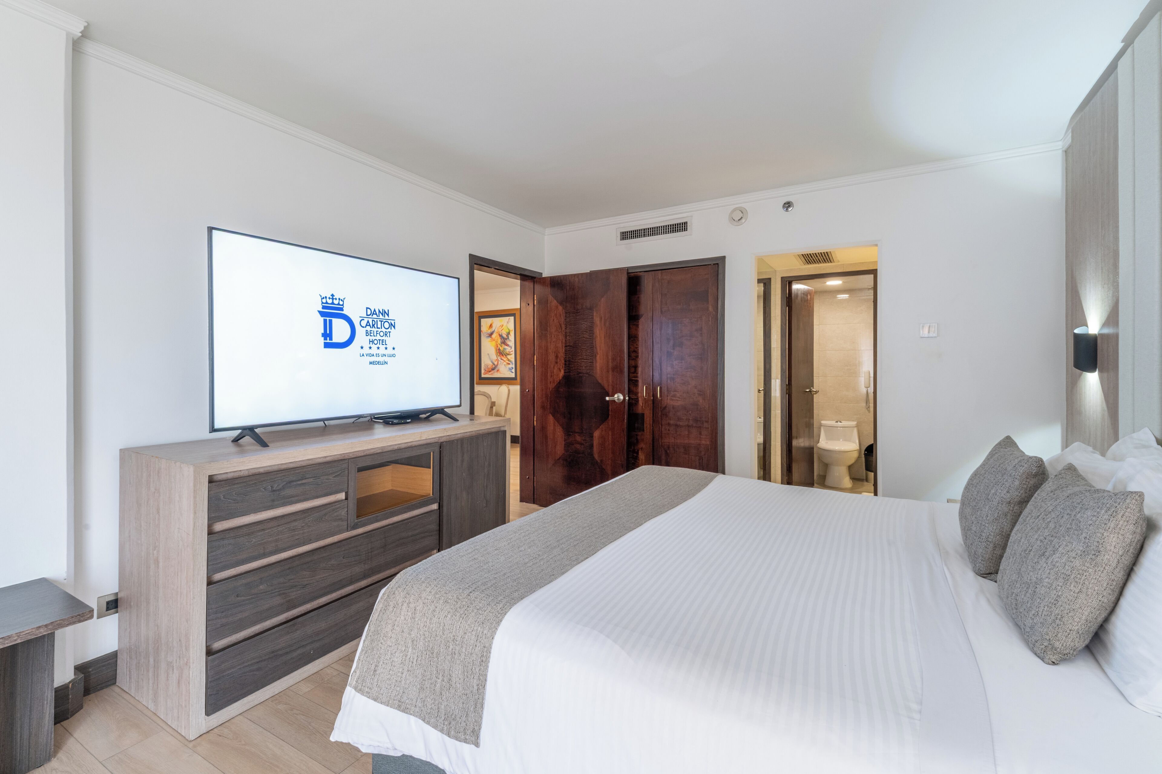 A hotel room with a bed, a TV, a wardrobe, and a bathroom visible through an open door.