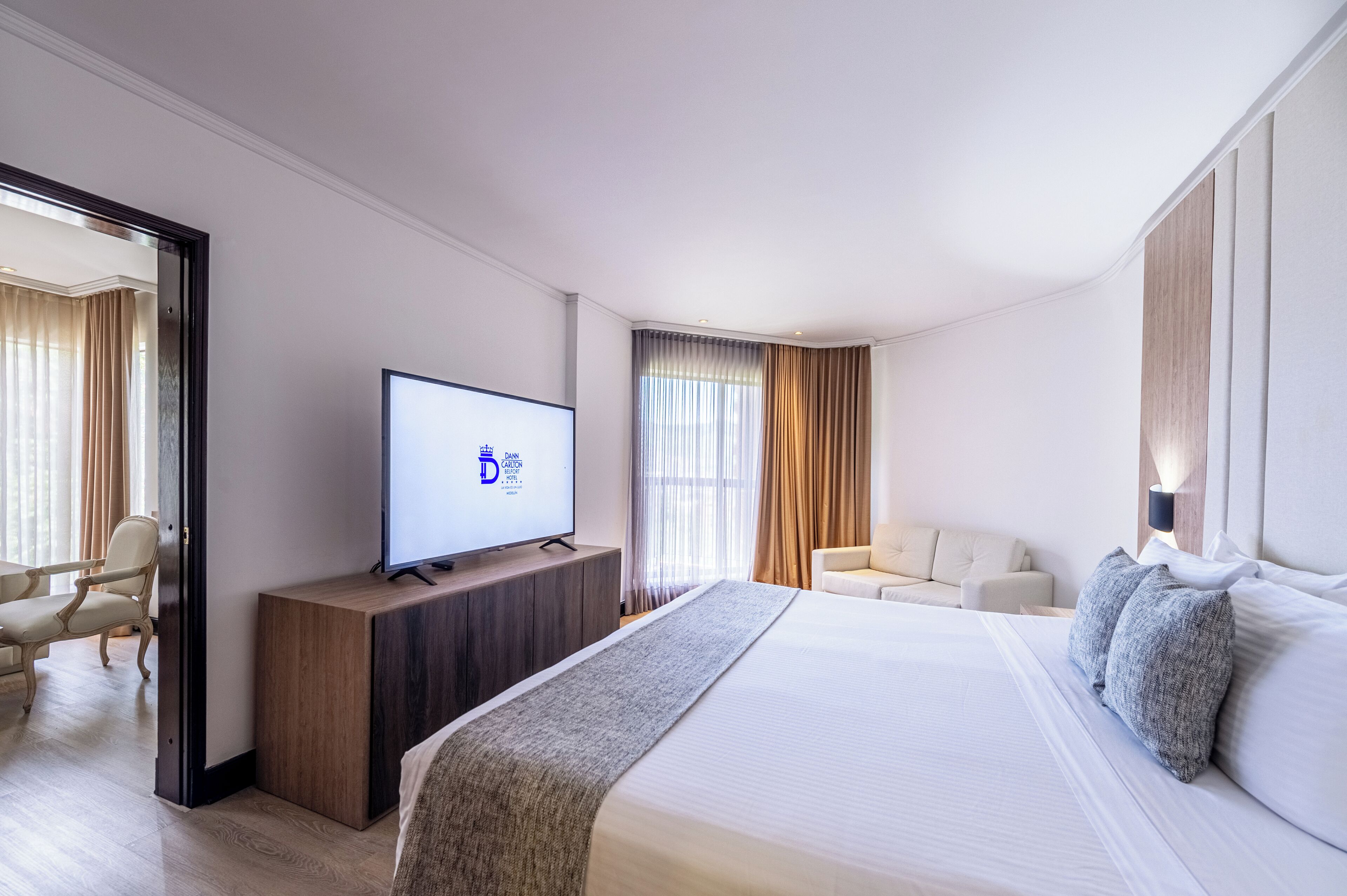 A hotel room with a large bed, a TV on a wooden stand, a sofa, and a desk.