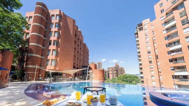 A rooftop pool area with a breakfast setup, including plates, cups, and juice. - Hotel Dann Carlton Belfort Medellin (Medellín)
