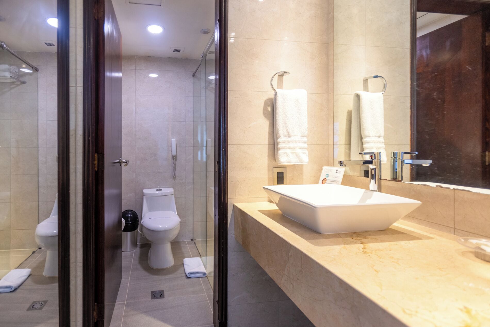 Un baño moderno con ducha de vidrio, un lavamanos blanco y dos inodoros.