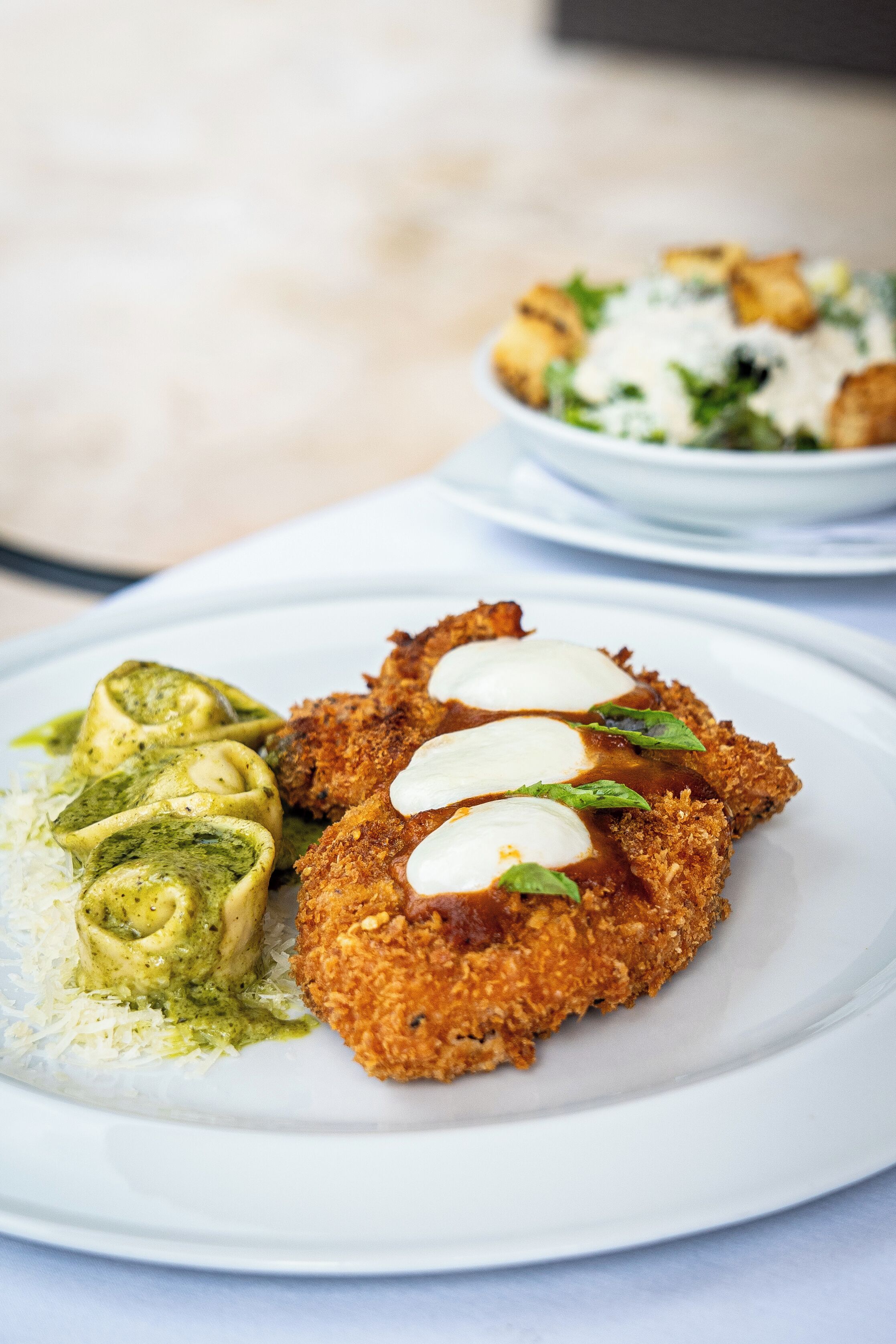 Ein Teller mit einem panierten Schnitzel, grüner Soße und geriebenem Käse.