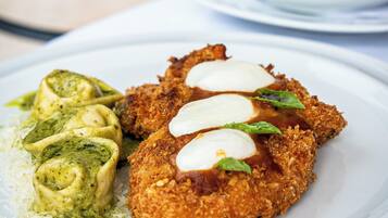 Ein Teller mit einem panierten Schnitzel, grüner Soße und geriebenem Käse.
