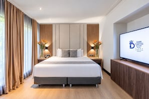 A hotel room with a large bed, wooden panel walls, a flat-screen TV, and a nightstand with a vase of flowers. - Hotel Dann Carlton Belfort Medellin (Medellín)