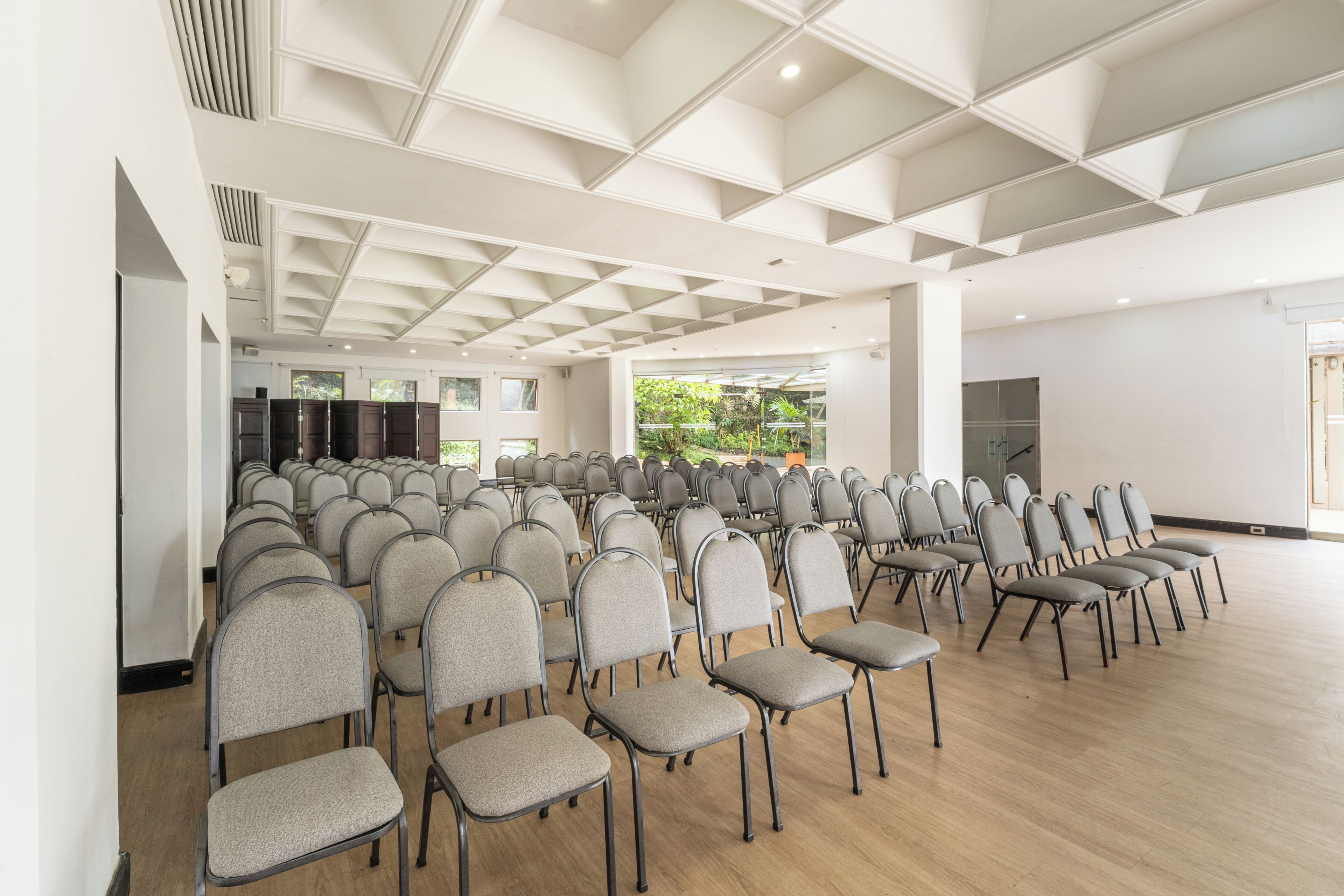 A conference room with rows of chairs, a wooden floor, and a white ceiling with geometric patterns.