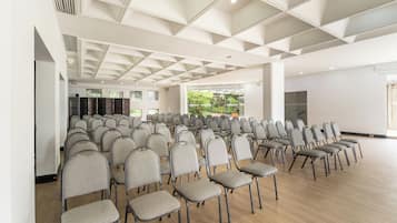 A conference room with rows of chairs, a wooden floor, and a white ceiling with geometric patterns.
