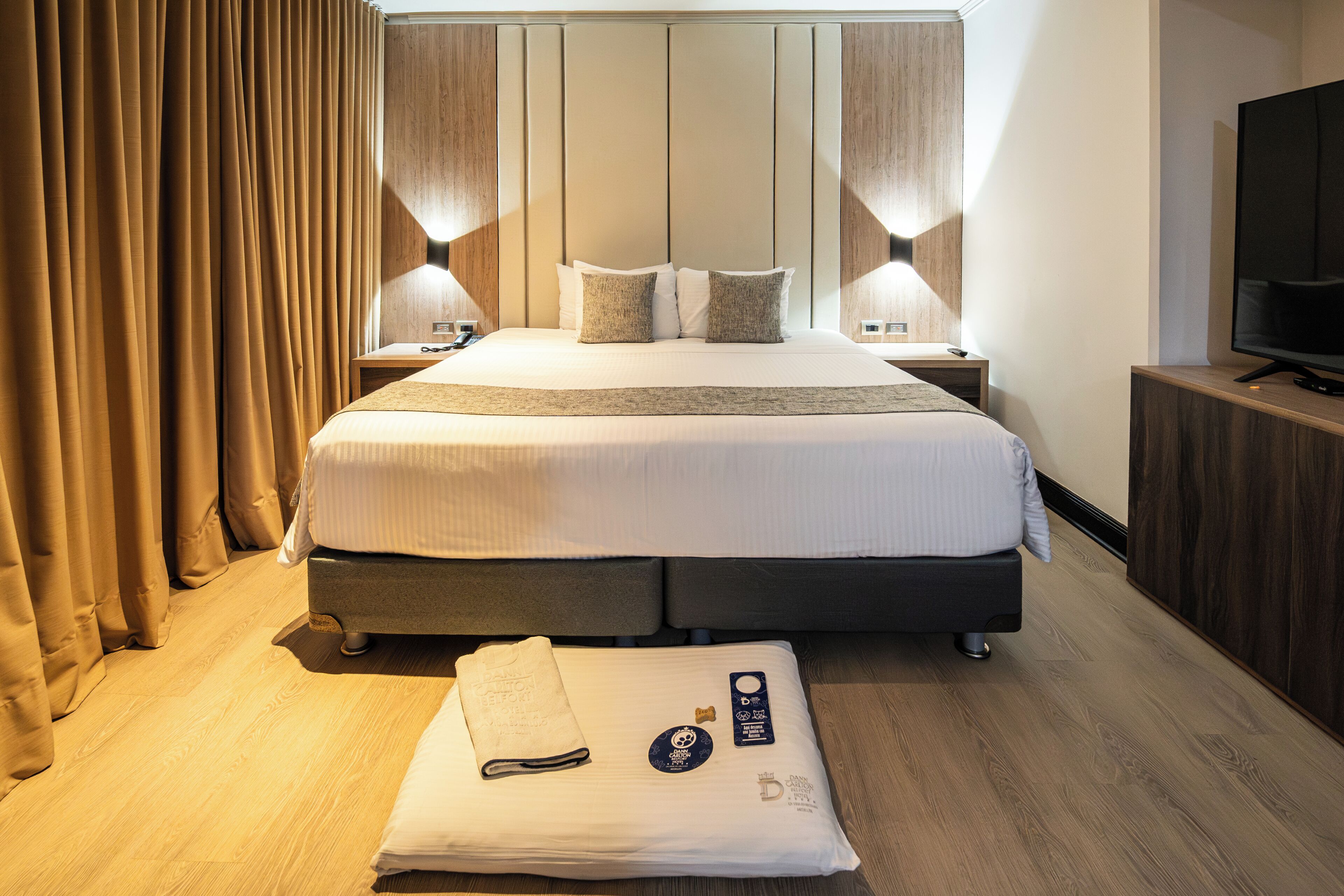 Una habitación de hotel con una cama grande, dos mesitas de noche, un televisor y suelo de madera.
