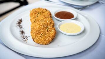 A plate with a breaded item, two dipping sauces, and a small bowl of oil.