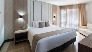 A modern hotel room with a large bed, bedside tables, a sofa, and a view of the city through the window. - Hotel Dann Carlton Belfort Medellin (Medellín)