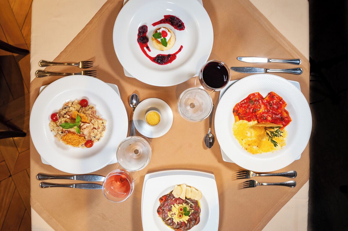 A table set with four plates of food, two glasses of red wine, and a small bowl of lemon.