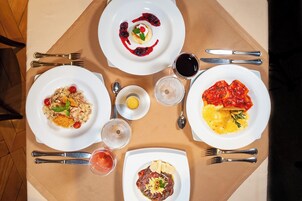 A table set with four plates of food, two glasses of red wine, and a small bowl of lemon.