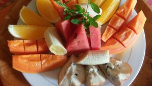 A plate of sliced fruits including watermelon, oranges, and bananas, arranged on a wooden table. - Polish Princess Guest House (Port Antonio)
