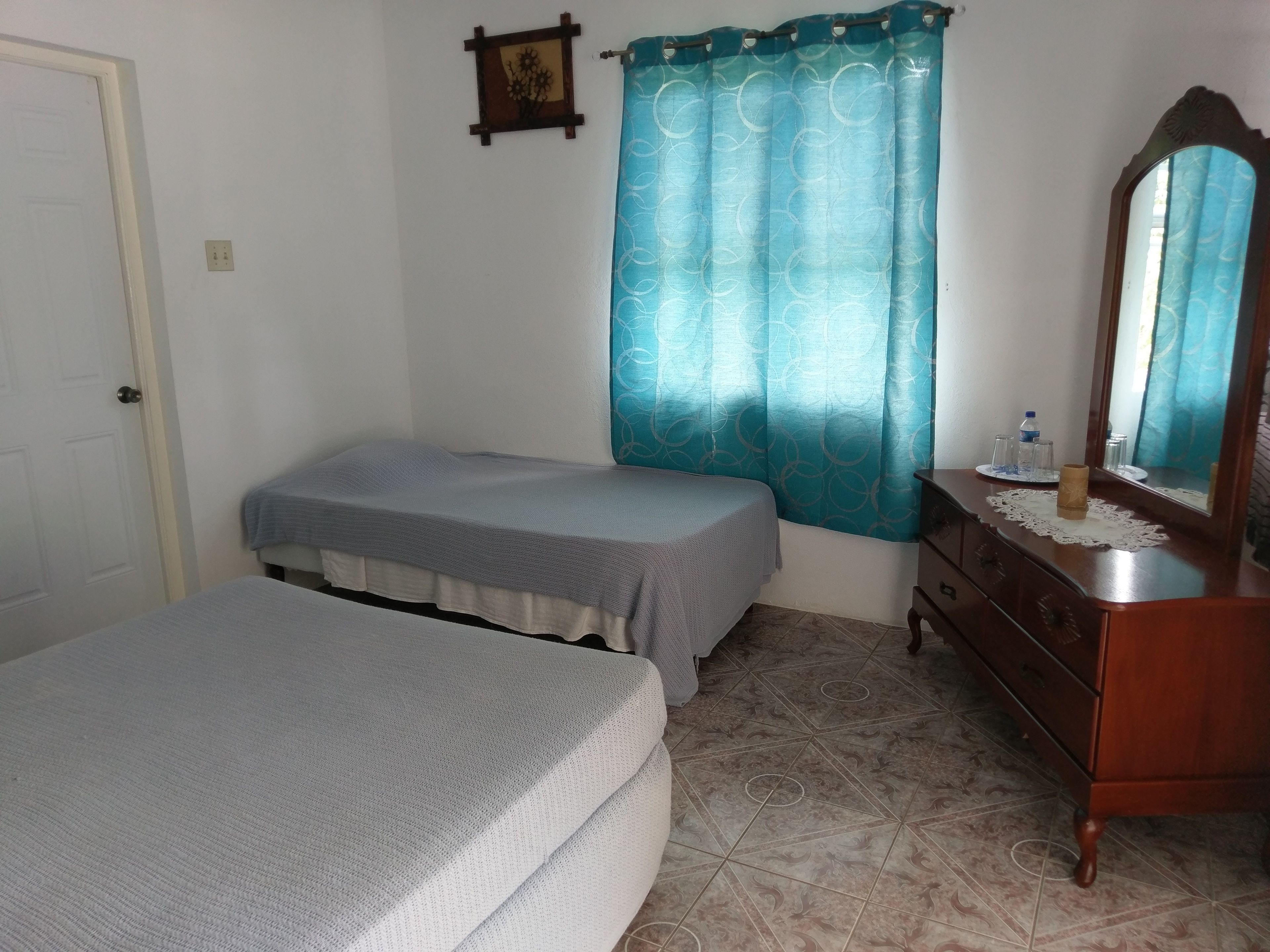 A bedroom with a bed, a dresser, a mirror, a curtain, and a wall-mounted picture.