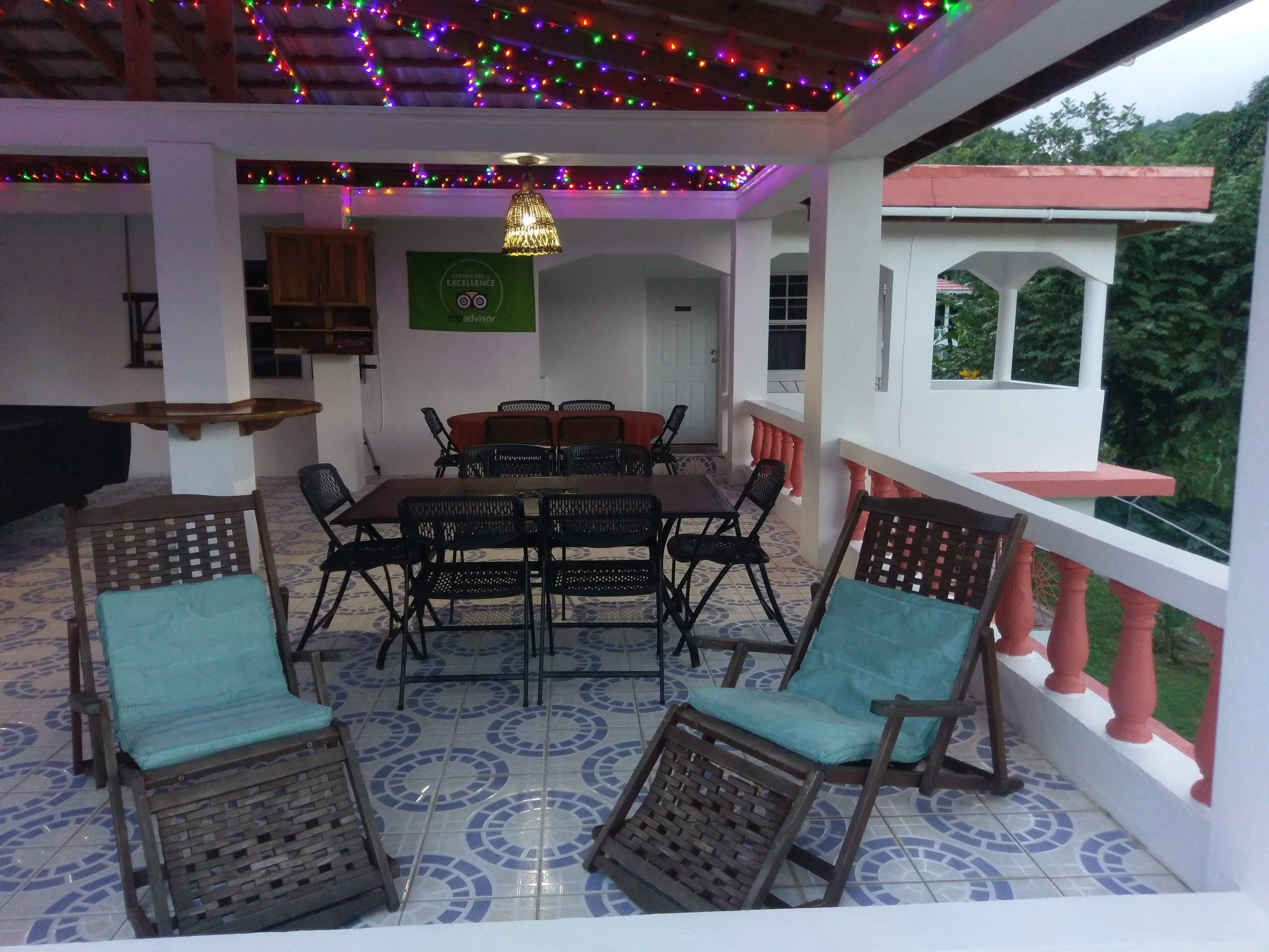 A covered patio area with a dining table and chairs, surrounded by a railing and a view of greenery.